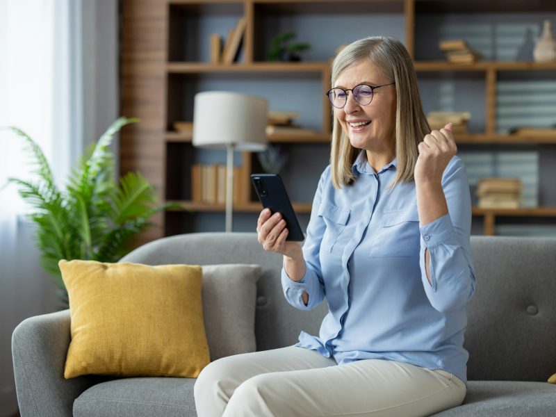 Joyful senior woman celebrating a win with smartphone